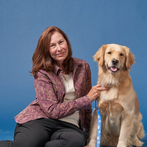 Picture of Darleen Harmon sitting to the left of Tallie (golden retriever) with blue background